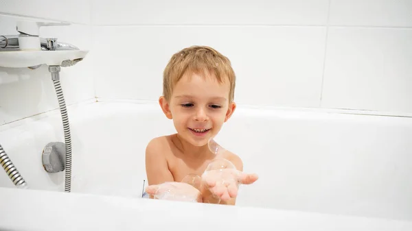 Retrato de menino bonito segurando bolhas de sabão na mão enquanto toma banho — Fotografia de Stock