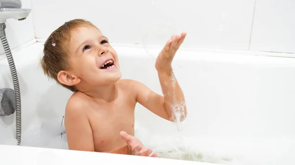 Feliz niño sonriente jugando con burbujas de jabón y espuma en el baño — Foto de Stock