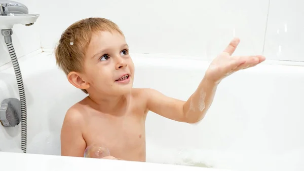 Retrato de niño lindo captura burbuja de jabón mientras se lava en el baño — Foto de Stock