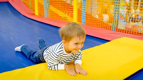 Retrato de feliz rindo menino deitado em tramploine no parque de diversões — Fotografia de Stock
