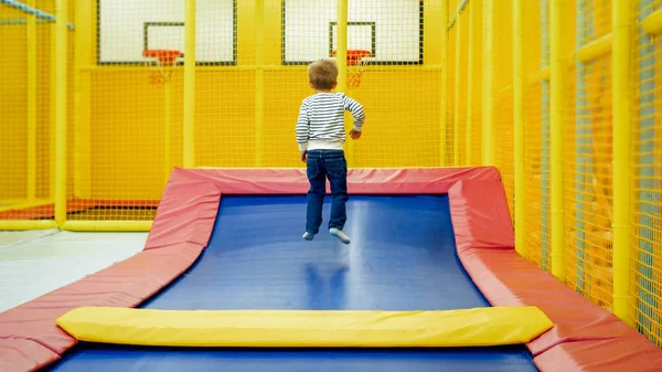 Rear view photo of little boy jumping and having fun on trampoline at amusement park — Stock Photo, Image