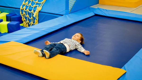 Bonito menino cansado deitado no trampolim depois de pálido e pulando no playground — Fotografia de Stock