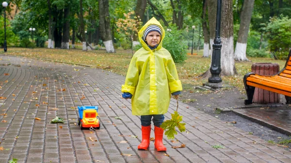 Malý batole kluk v pláštěnce a gumových botách se naštval kvůli špatnému počasí a silnému dešti v parku — Stock fotografie