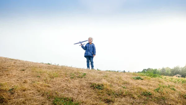 Glücklich lächelnder kleiner Junge steht mit Spielzeugflugzeug auf Hügelkuppe — Stockfoto