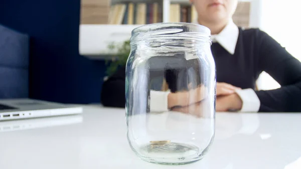 Closeup image of business lady dressed in black dress ,sitting at the white table on which is located empty of coints jar — Stock Photo, Image