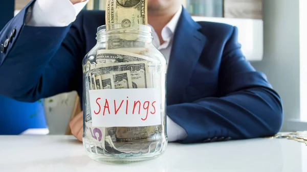 Empresário colocando dinheiro em jarra de vidro para economizar. Conceito de investimento financeiro, crescimento económico e poupança bancária — Fotografia de Stock