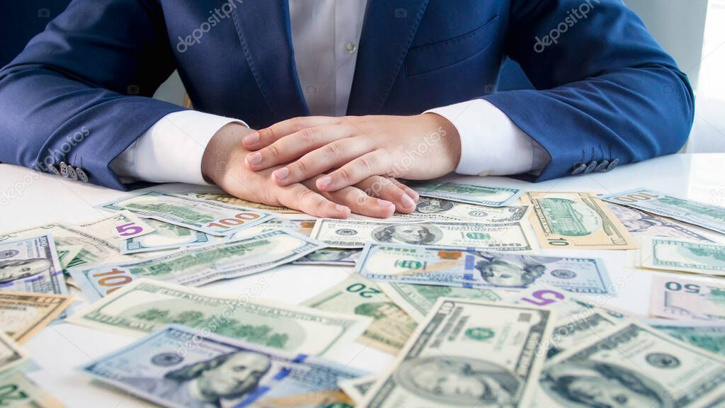 Male businessman holding hands on desk covered with money. Concept of financial investment, economy growth and bank savings