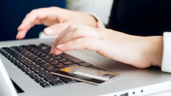 Plastic credit card lying on laptop keyboard while young woman browsing internet — Stock Photo, Image