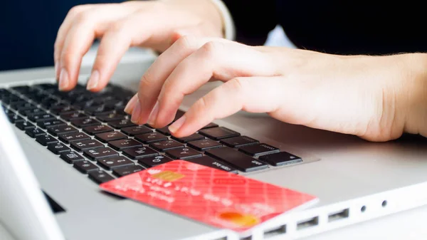 Bank credit card lying on laptop next to female hands typing on keyboard. Concept of online shopping and e-commerce — Stock Photo, Image