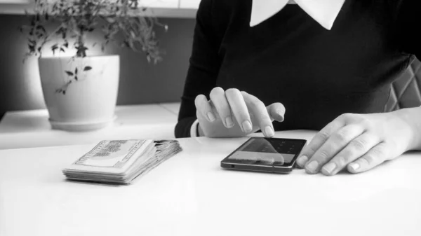 Schwarz-Weiß-Foto einer Geschäftsfrau, die mit Taschenrechner auf dem Smartphone Geld prägt, — Stockfoto