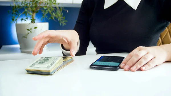 Joven empresaria sosteniendo fajo de dinero utilizando la calculadora en el teléfono inteligente — Foto de Stock