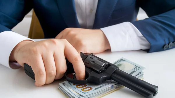 Closeup image of male businessman or criminal holding gun on wad of cash