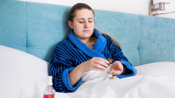 Sick young woman lying in bed and holding pills on hand — Stock Photo, Image