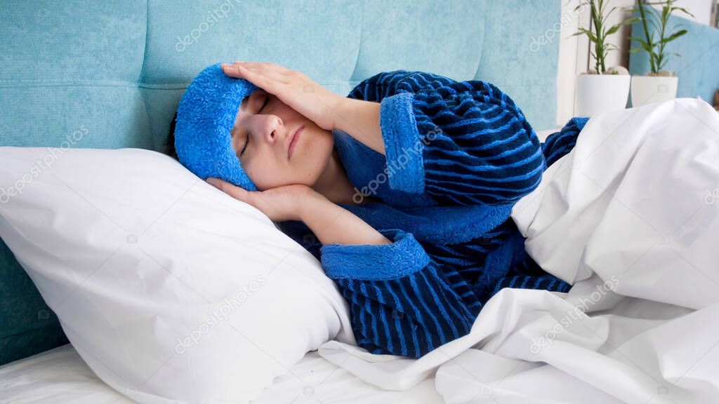 Portrait of young woman with headache lying in bed with cold compress on head