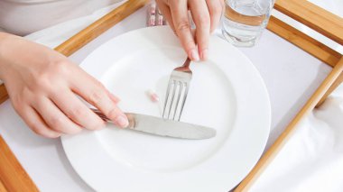 Kadın boş tabaktan çatal ve bıçakla hap alıyor. Diyet, kilo kaybı ve ilaç kavramı