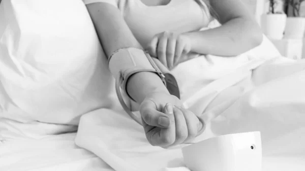 Imagen en blanco y negro de una mujer joven acostada en la cama y midiendo la presión arterial con un tonómetro digital — Foto de Stock