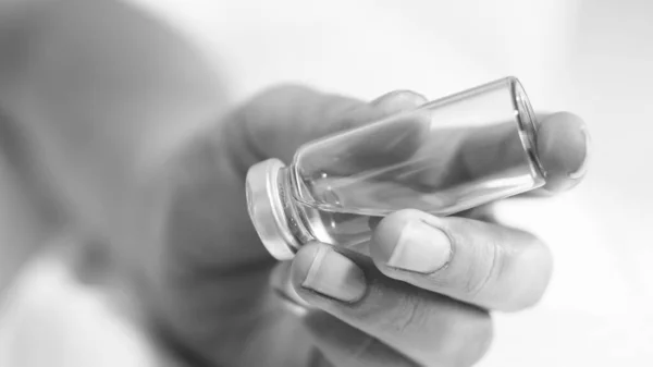 Zwart-wit beeld van een vrouwelijke verpleegkundige die een glazen injectieflacon met geneesmiddelen vasthoudt — Stockfoto