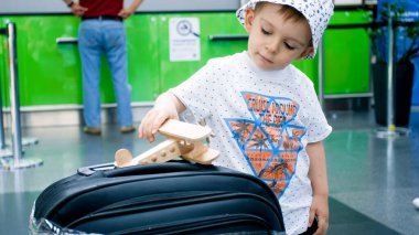 Uçuştan önce havaalanında oyuncak uçakla oynayan şirin bir çocuk.