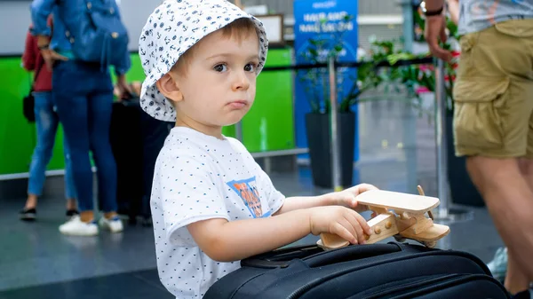 Porträtt av en liten pojke som leker med leksaksflygplan och resväska i flygplatsterminalen — Stockfoto