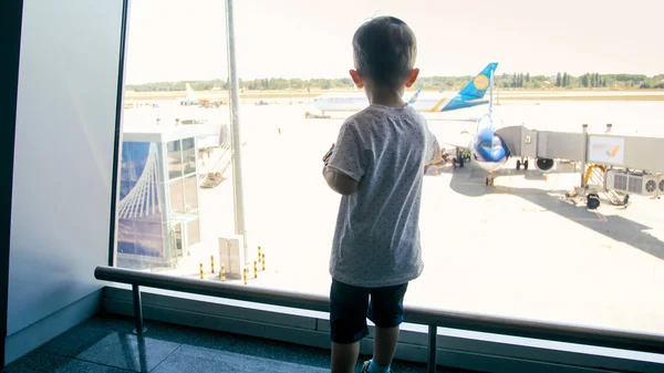 Imagem da visão traseira do menino bonito olhando através da janela do terminal do aeroporto — Fotografia de Stock