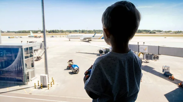 Silhuett av liten pojke tittar på flygplatsen landningsbana genom fönstret — Stockfoto