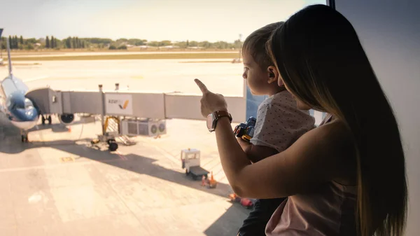 Imagen tonificada de una joven madre mostrando aviones en la pista del aeropuerto a su pequeño hijo — Foto de Stock