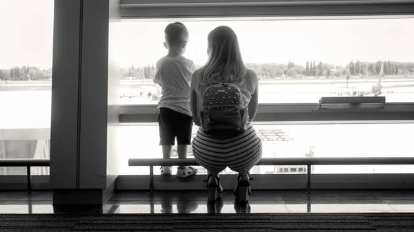 Černá a bílá silueta mladé matky s malým synem stojící u okna v letištním terminálu — Stock fotografie