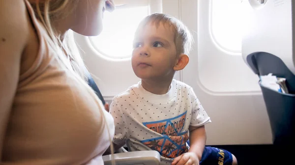 Retrato de un lindo niño mirando a su madre sentada en un avión — Foto de Stock