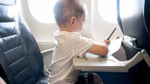 Netter kleiner Junge zeichnet Bild mit Bleistiften während er im Flugzeug fliegt — Stockfoto