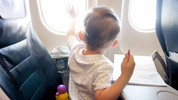 Netter kleiner Junge schaut während des Fluges im Flugzeug aus dem Fenster — Stockfoto