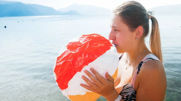 Izolovaný portrét usmívající se mladé matky foukající vzduch v nafukovací plážový míč na moři — Stock fotografie