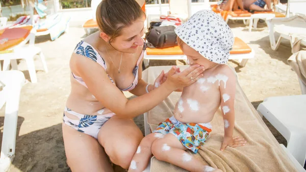 Retrato de una joven madre sonriente protegiendo la piel de sus hijos de la luz solar UV con loción de protector solar —  Fotos de Stock