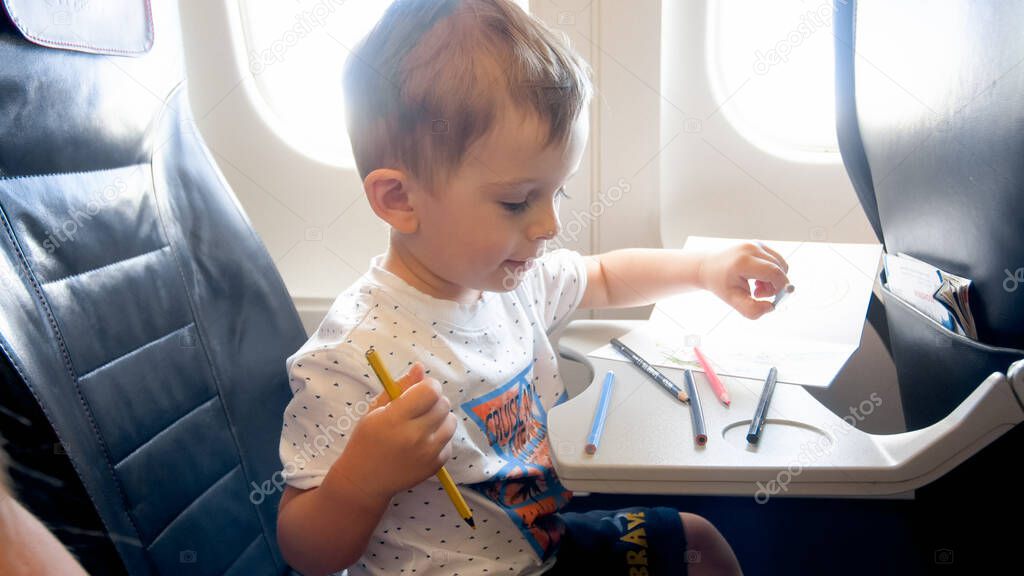 Portrait of smiling toddler boy drawing with pencils during flight in airplane