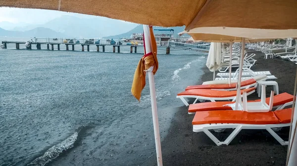 Мокрые шезлонги и зонтики на морском пляже во время сильного дождя — стоковое фото