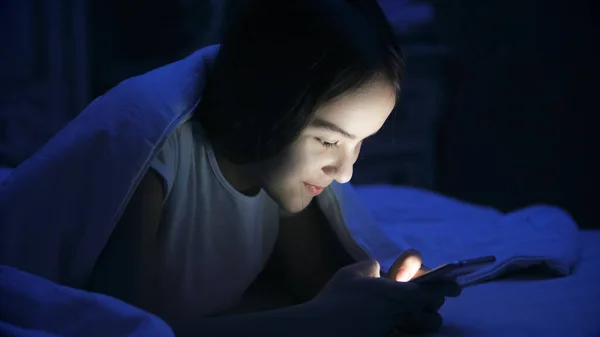 Portrait of teenage girl lying in bed and using smartphone — Stock Photo, Image