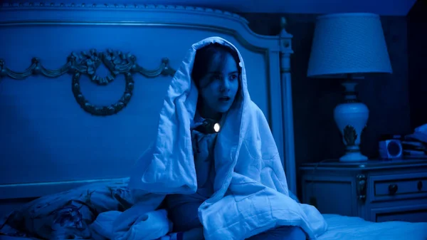 Scared little girl hiding under blanket at night and looking for monsters — Stock Photo, Image