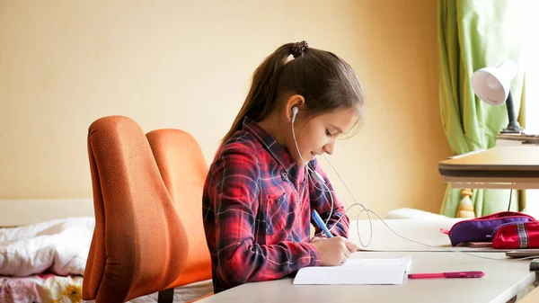 Porträtt av glad leende flicka lyssna på musik när du gör skolan läxor i sovrummet — Stockfoto