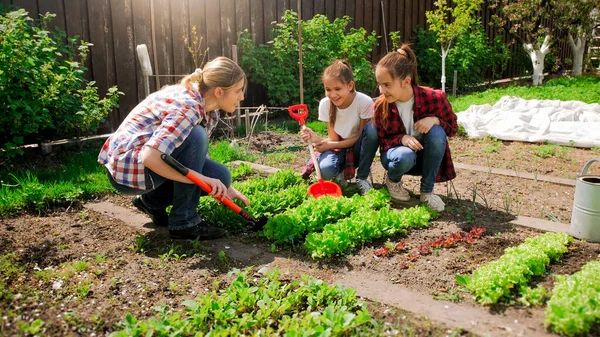 Jeune mère enseignant à ses enfants travaillant dans le jardin et plantant des semis — Photo