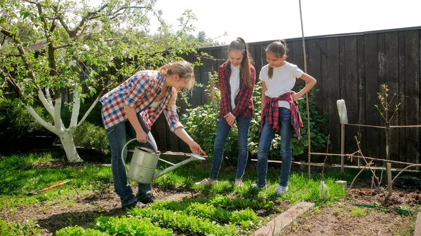 Mujer joven con dos hermanas adolescentes regando verduras en el jardín — Foto de Stock