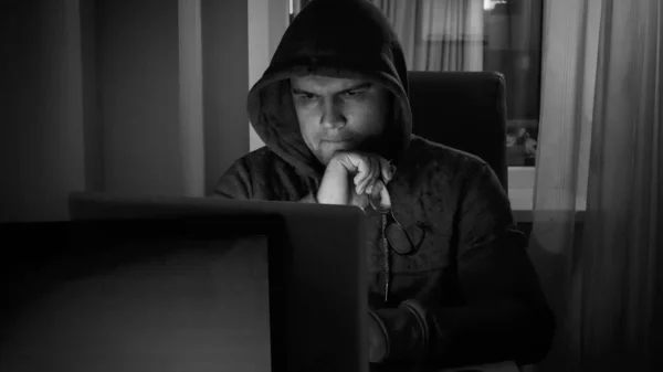 Ritratto in bianco e nero di hacker maschile in cappuccio che lavora al computer di notte — Foto Stock