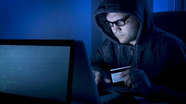 Mahalledeki erkek hacker 'ın elinde kredi kartı var ve online bankacılık sisteminden para çalıyor.