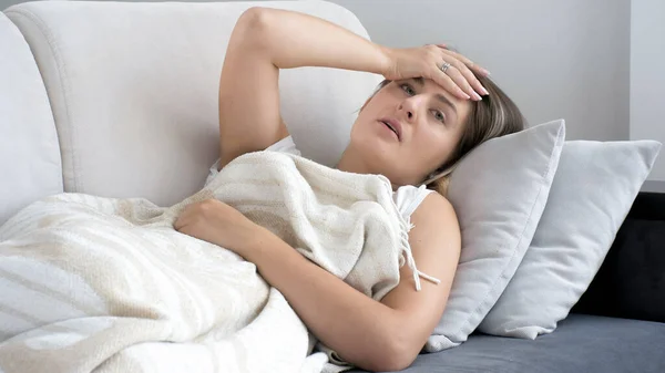 Portrait of woman suffering from migraine lying on sofa under blanket — Stock Photo, Image