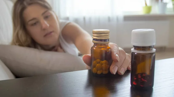Närbild av ung sjuk kvinna sträcker sig efter piller på nattduksbordet — Stockfoto