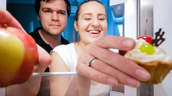 La giovane coppia affamata che prende il cibo di frigorifero per spuntino tardo di notte — Foto Stock