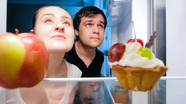 Portrait of hungry man and woman looking for something to eat in fridge at night — Stock Photo, Image