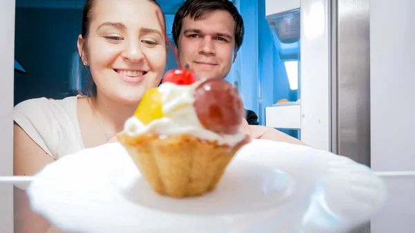 Familia sonriente sacando pastel dulce de la nevera en la cocina por la noche. Concepto de dieta y nutrición saludable — Foto de Stock