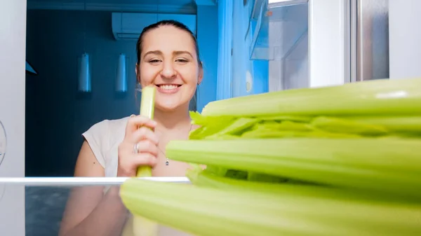 Uśmiechnięta młoda kobieta na diecie jedząca świeży seler na przekąskę w nocy. Pojęcie diety i zdrowego odżywiania — Zdjęcie stockowe