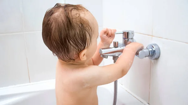 Lindo niño abre el grifo de agua en el baño mientras se baña — Foto de Stock