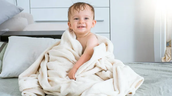 Bebê sorridente em toalha branca depois de tomar banho sentado na cama — Fotografia de Stock