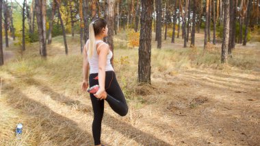 Ormanda spor yapmadan önce at kuyruklu, ısınan ve esneyen seksi genç kadın.